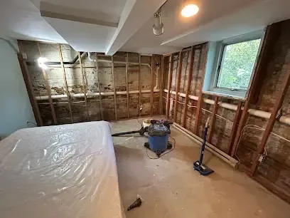 A room opened to the studs with plastic sheeting and a wet vacuum set up for drying