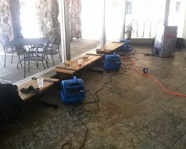 Air movers spread over a wet floor with the furniture pushed aside during structural drying